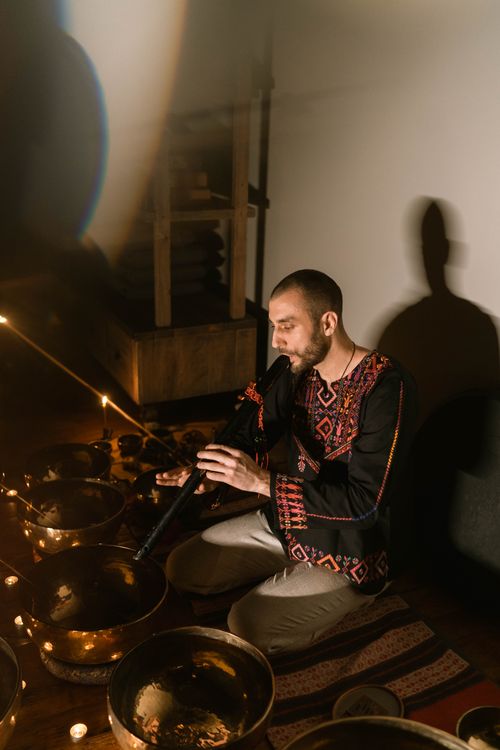 Free A man playing a flute surrounded by Tibetan singing bowls in a serene indoor setting. Stock Photo