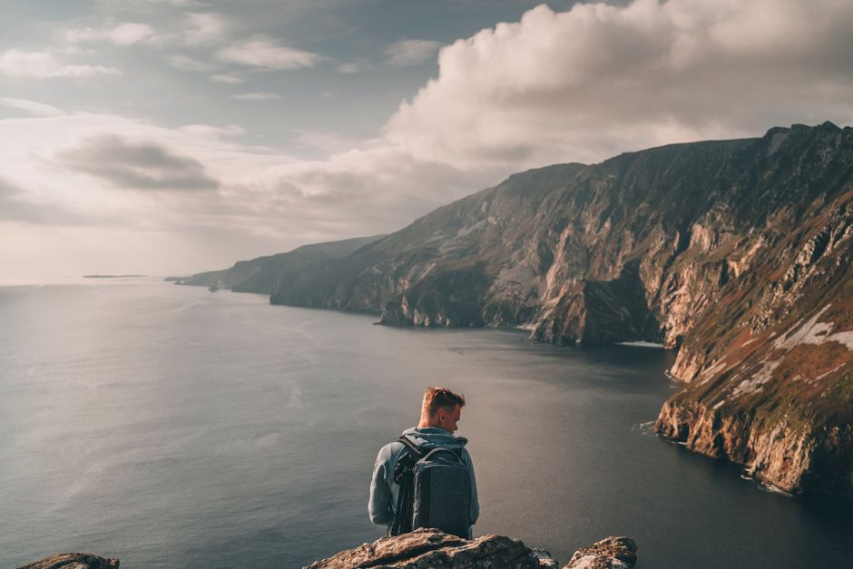 Traveler enjoying the stunning coastal cliffs of Ireland under a cloudy sky.