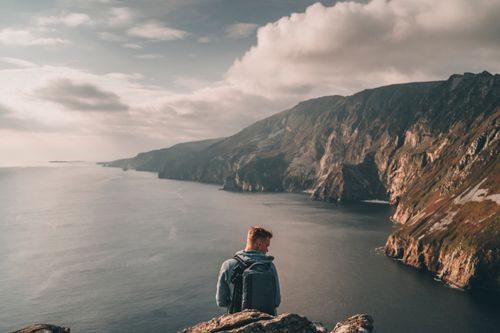 Free Traveler enjoying the stunning coastal cliffs of Ireland under a cloudy sky. Stock Photo