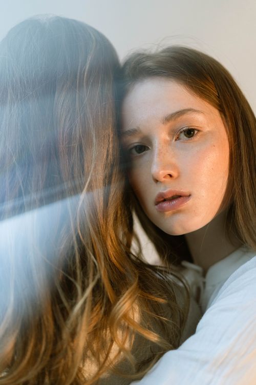 Free A thoughtful portrait of a young woman with reflective glass indoors, capturing soft lighting and an intimate mood. Stock Photo