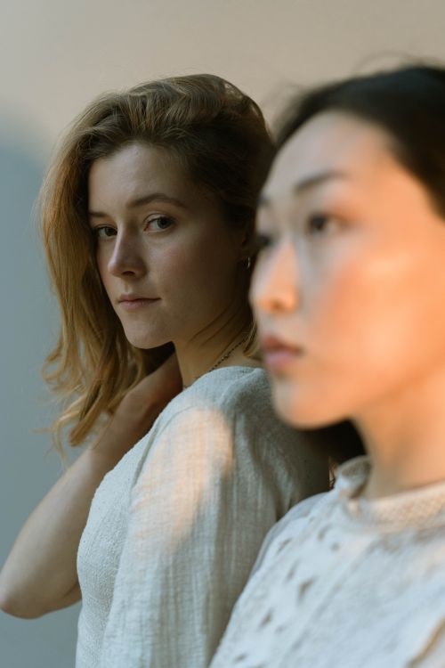 Free A graceful portrait capturing two young women in soft lighting, showcasing diversity. Stock Photo