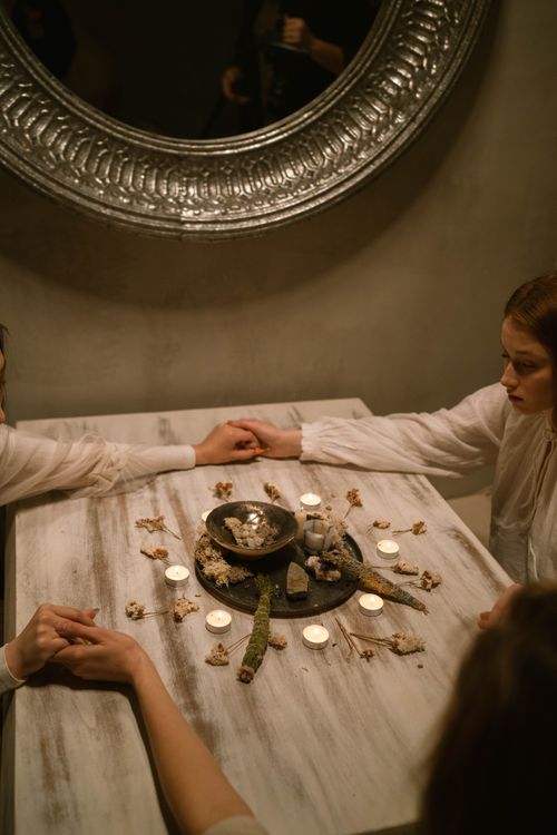 Free A spiritual ritual scene with people holding hands around a candle-lit table adorned with dried flowers. Stock Photo