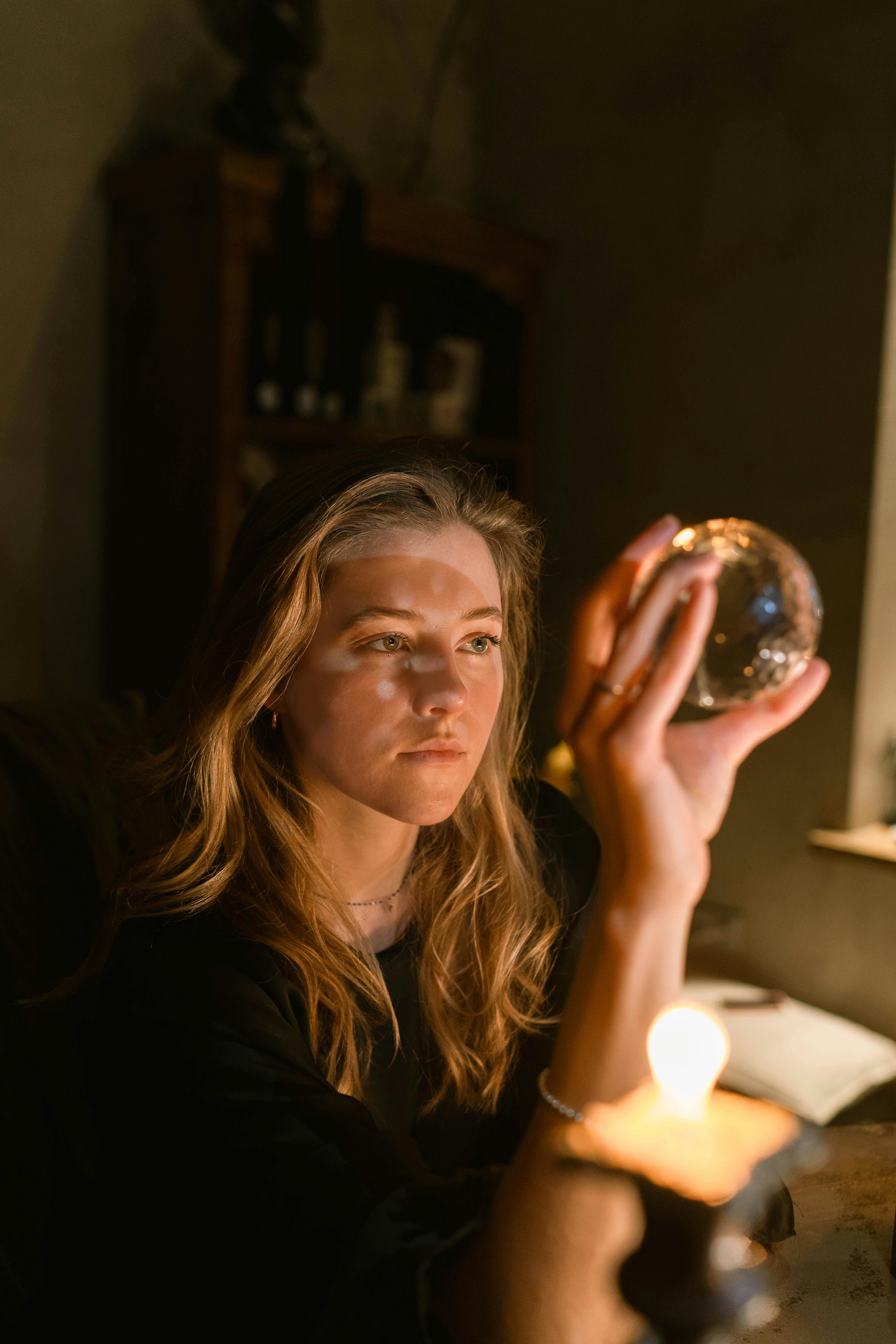 A contemplative woman explores fortune telling with a crystal ball in a dimly lit room.