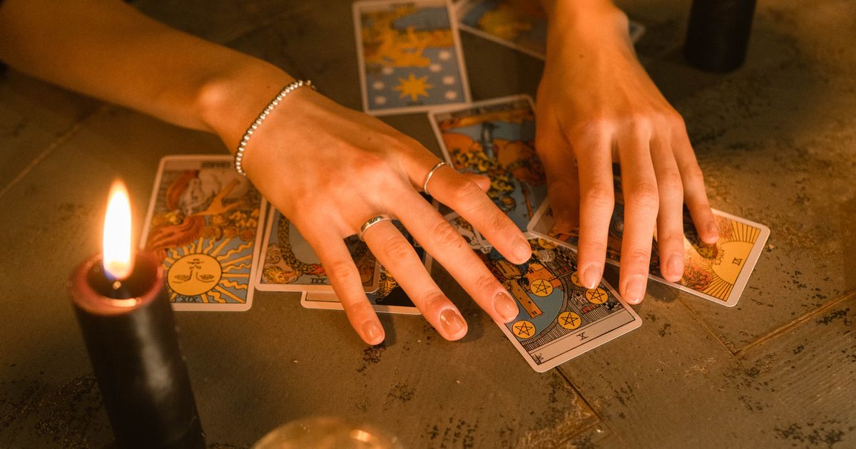 Hands resting beside tarot cards, candles, and a crystal ball on a dark table, representing reading two Destiny Matrix charts together for compatibility