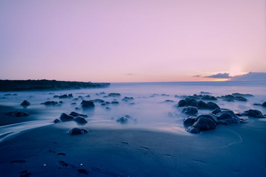 A tranquil beach scene with misty rocks and a pink sky during sunset.