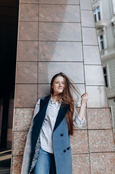 Young happy female in stylish outfit looking away and smiling near building with modern tile