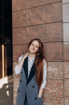 Young positive female with long hair in stylish outfit looking at camera near modern shiny wall
