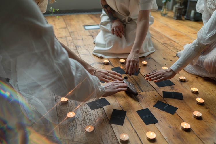 People Sitting On The Wooden Flooring While Putting Their Hands Above The Wooden Figurine