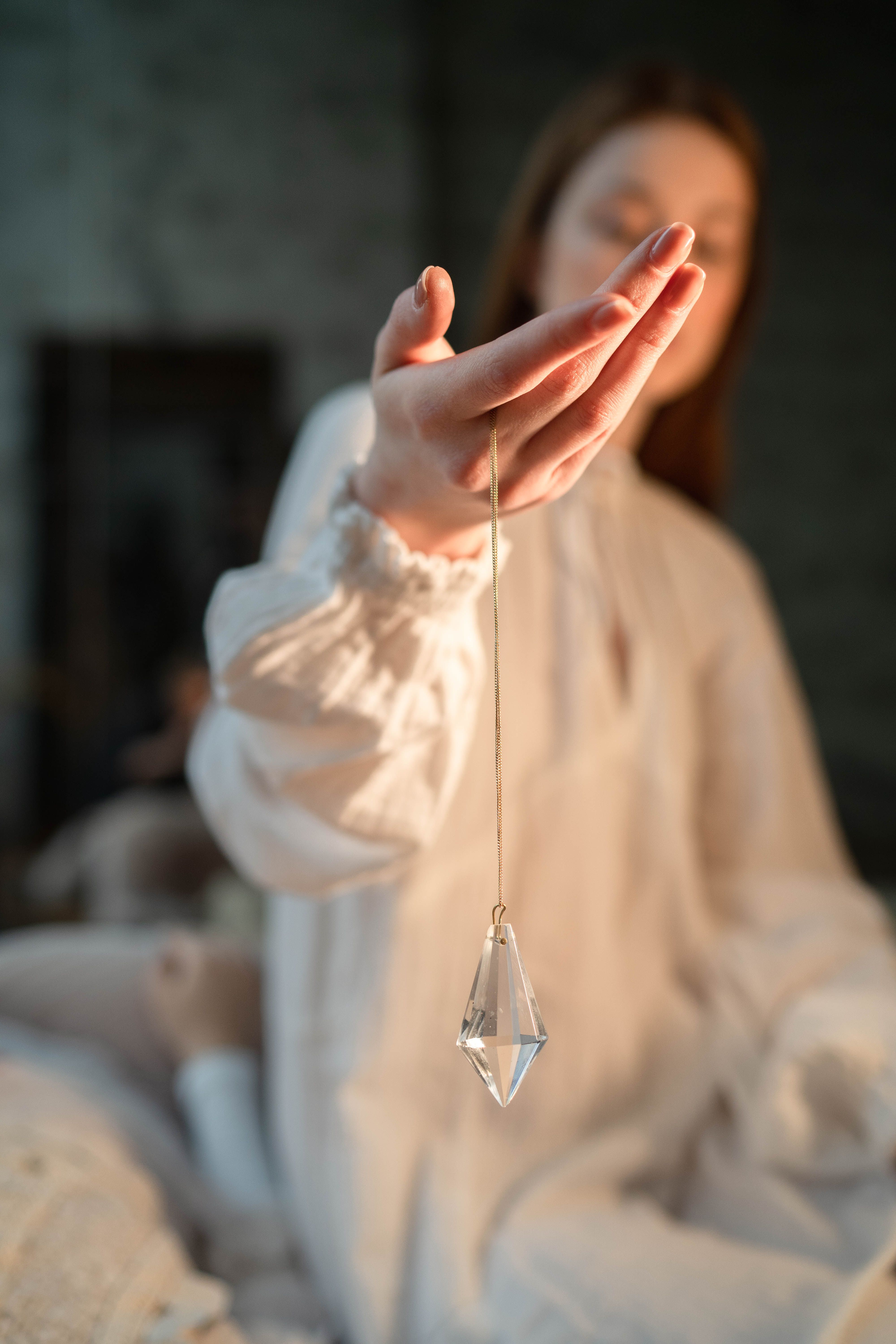 A woman holding a crystal pendant delicately in her hand, dressed in white.
