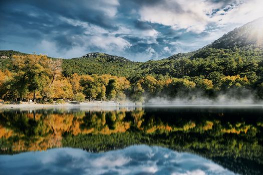 Captivating view of a tranquil lake in İzmir, Turkey, reflecting lush greenery and mountains under a vivid sky.