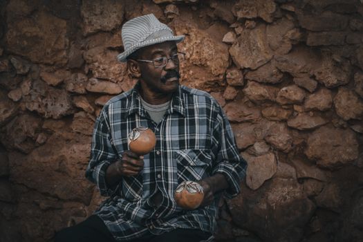 Pensive mature Hindu male in eyeglasses and hat looking away with ornamental balls against rough wall — photo by Mehmet Turgut  Kirkgoz