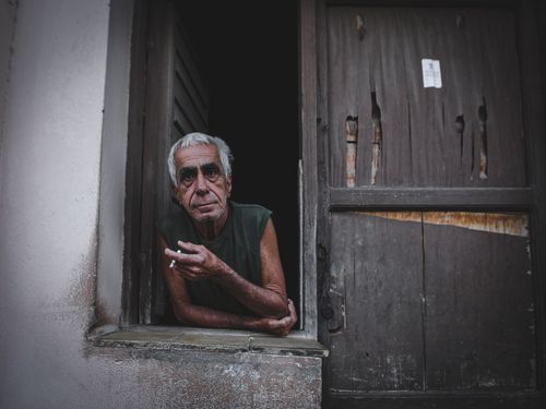 Free Senior ethnic male with gray hair and cigarette leaning on hand and looking forward from aged building Stock Photo