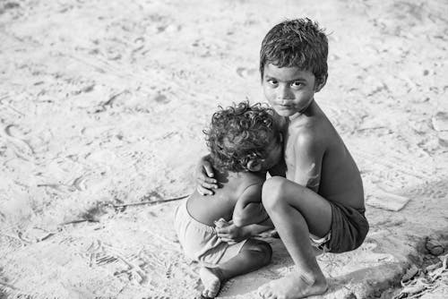 Grayscale Photo of Topless Boy Sitting on Sand