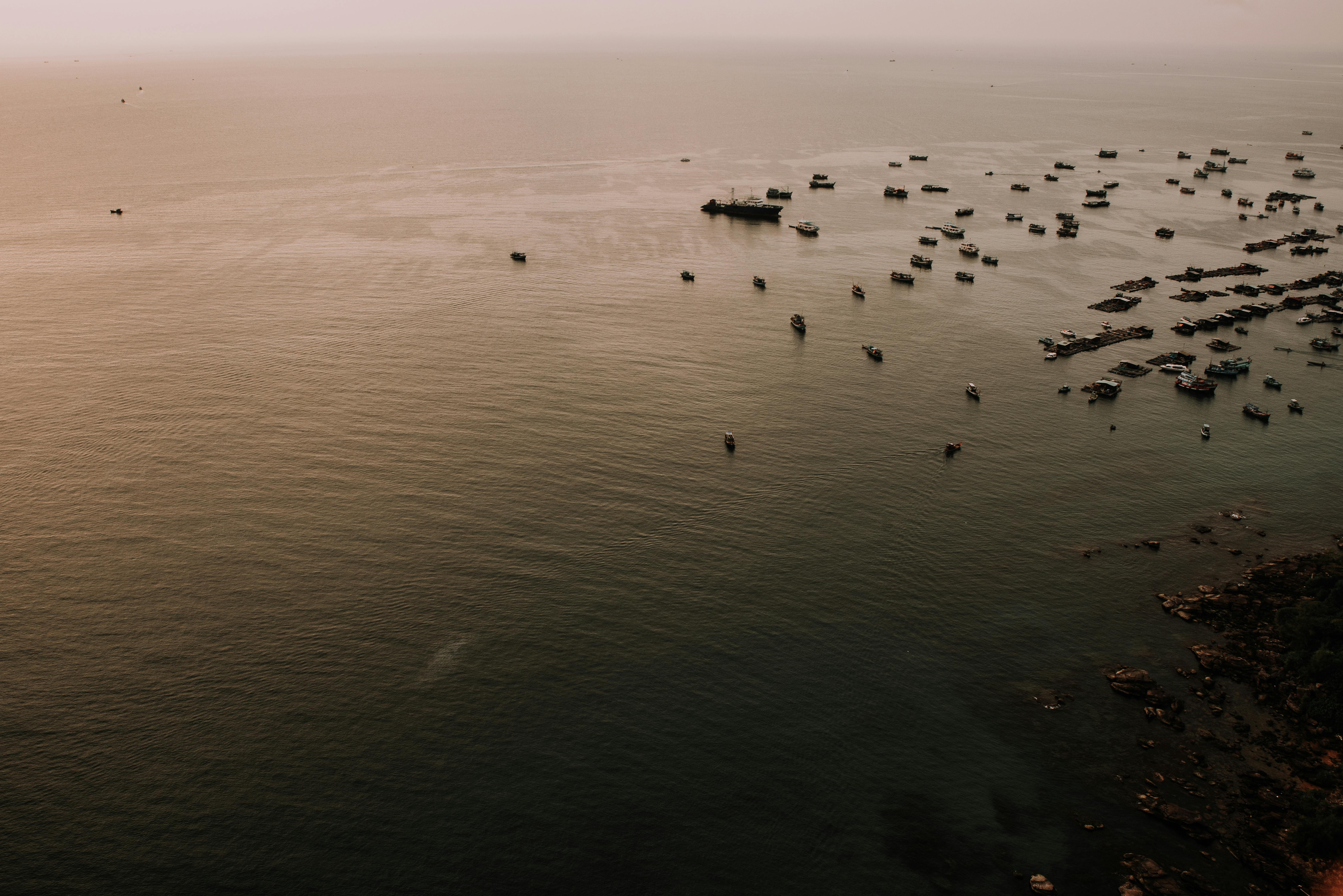 A serene aerial view of numerous boats on the water near a Vietnamese coastline during sunset.