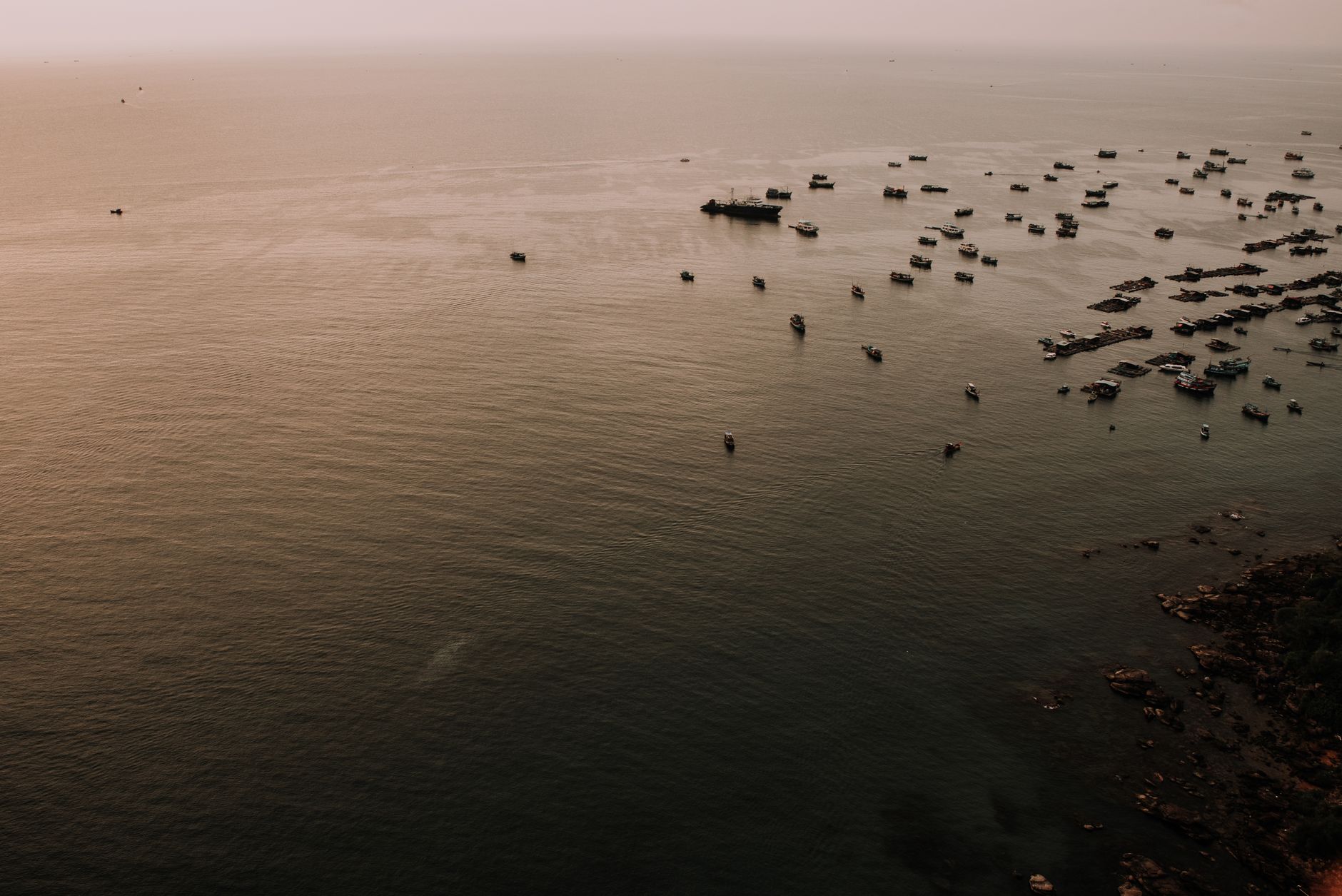 A serene aerial view of numerous boats on the water near a Vietnamese coastline during sunset.