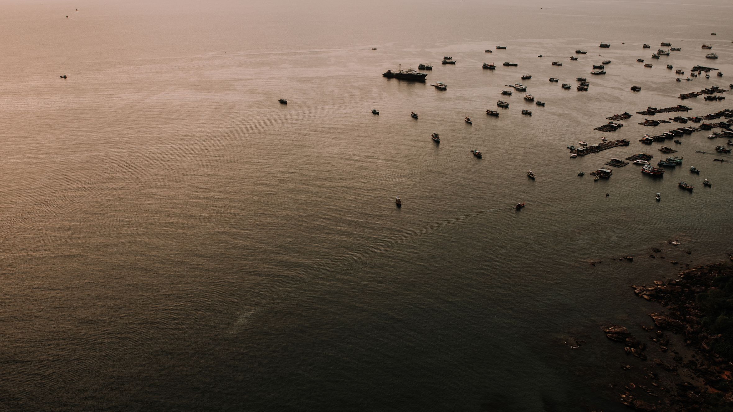 A serene aerial view of numerous boats on the water near a Vietnamese coastline during sunset.