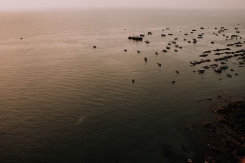 Free A serene aerial view of numerous boats on the water near a Vietnamese coastline during sunset. Stock Photo