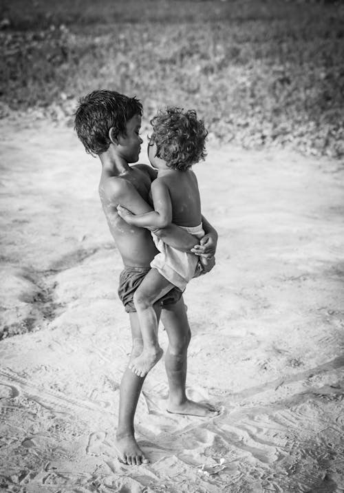 Grayscale Photo of a Boy Carrying a Child in White Shorts