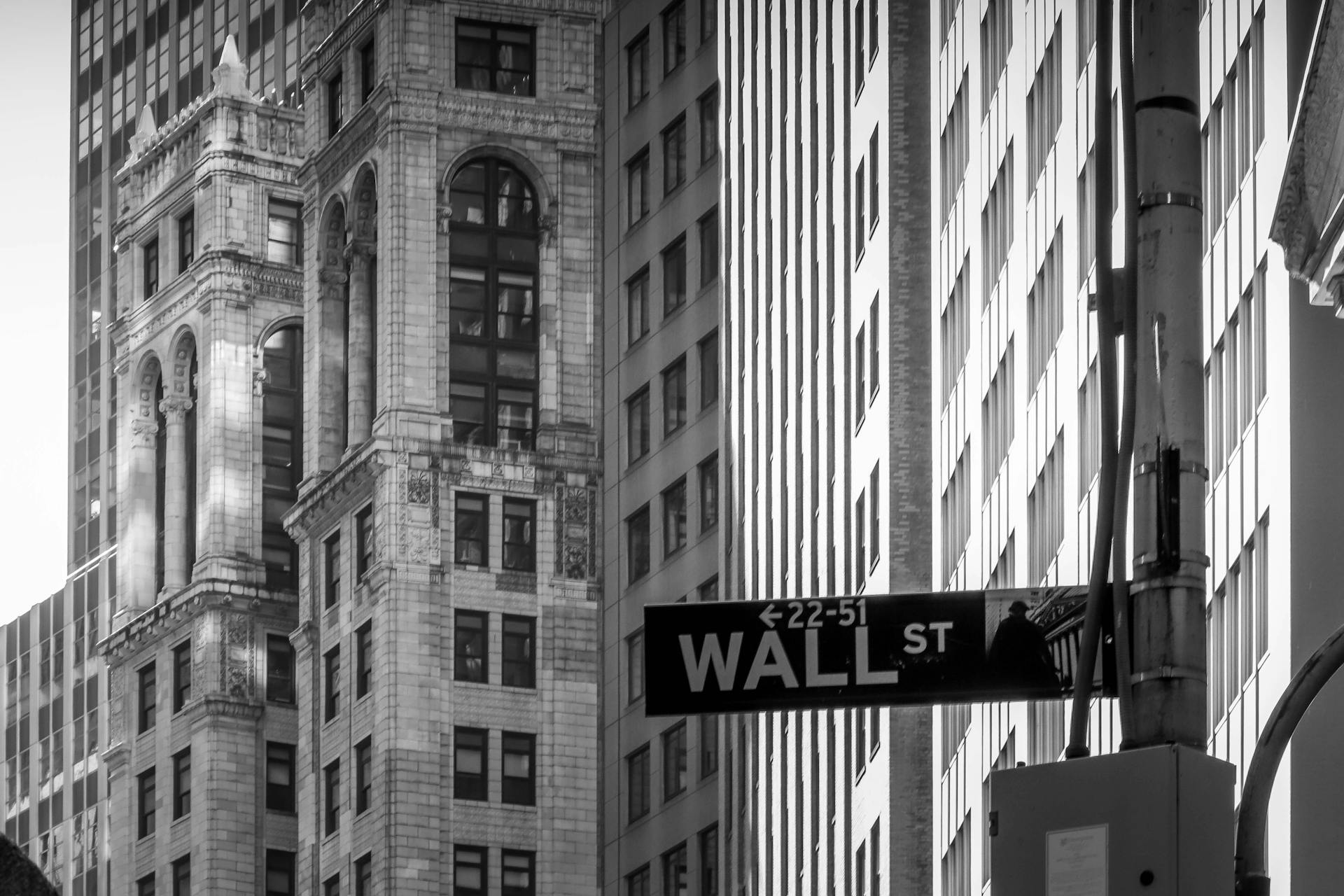 Black and white image capturing the iconic Wall Street, NYC architecture with street sign.