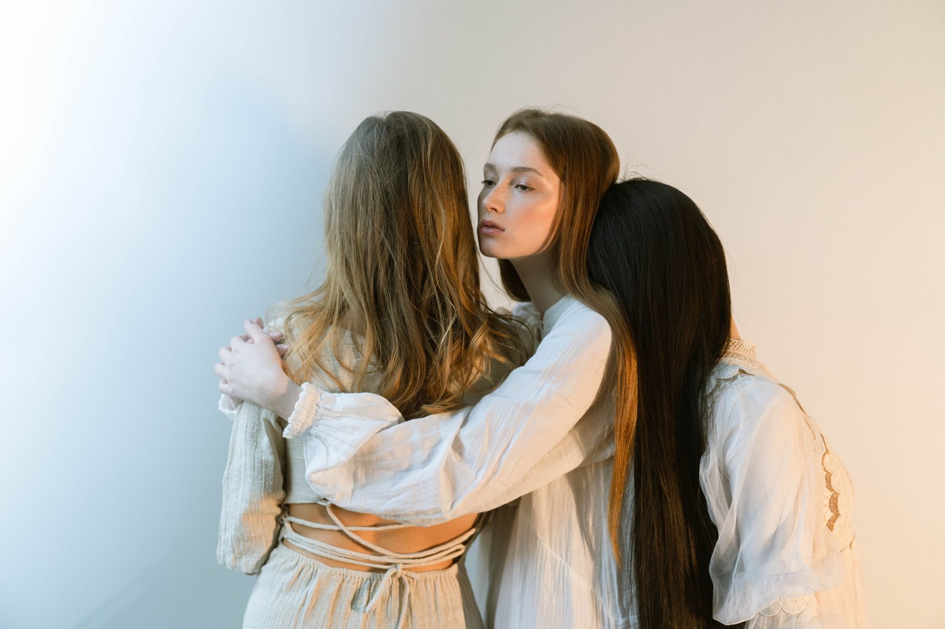 Three young women embracing each other in a serene indoor setting, evoking togetherness and empathy.