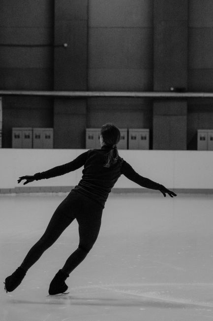 Black and white photo of a woman ice skating indoors, showcasing elegance and technique.
