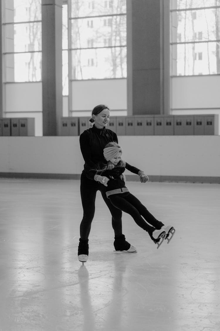 Grayscale Photo Of Woman Carrying The Girl While Ice Skating 