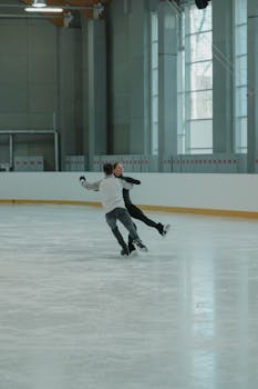 Couple performing figure skating moves on an indoor ice rink.