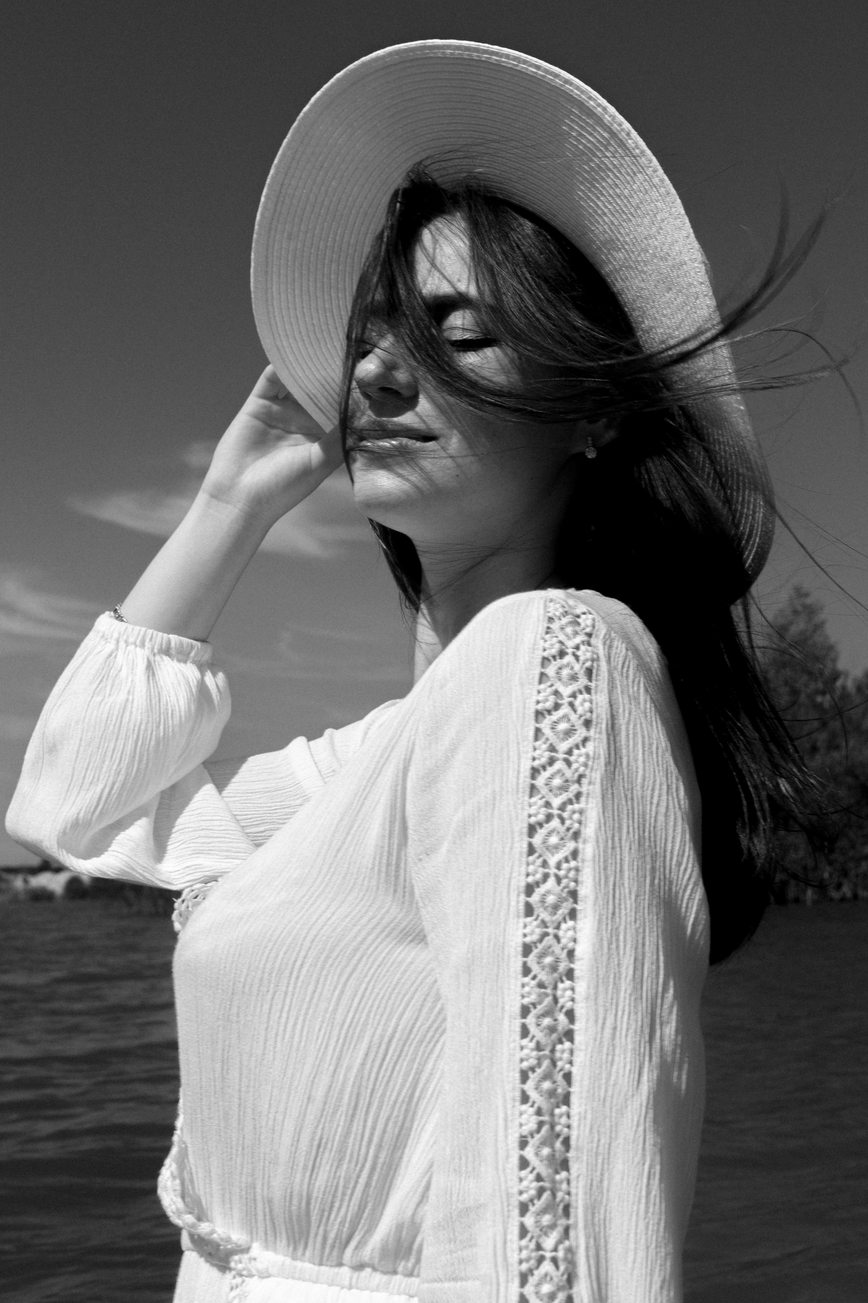 Side view of resting female with flying hair in hat and summer outfit near rippling water of sea