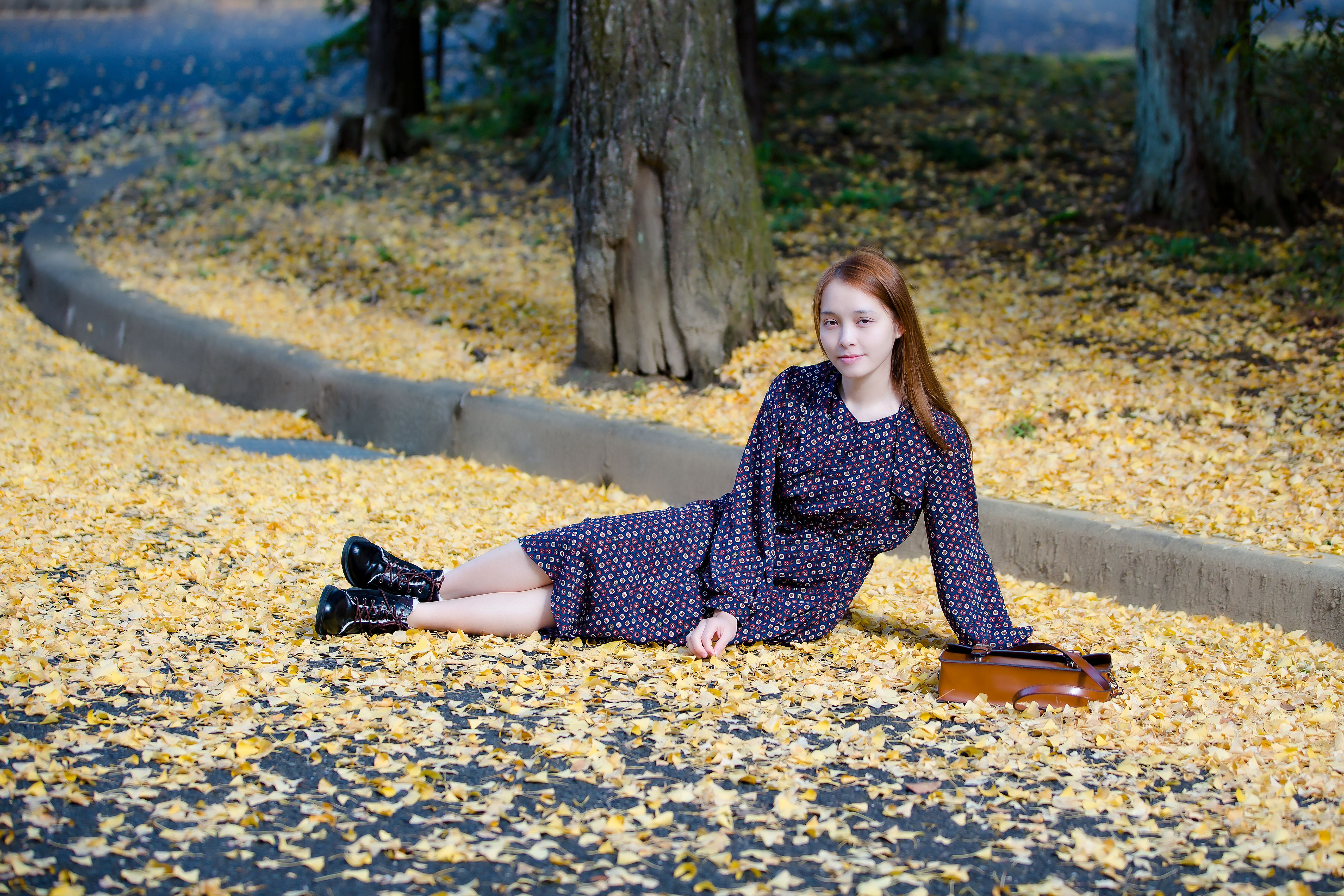 Woman in autumn dress sitting on a leaf-covered road, embracing the vibrant fall colors.