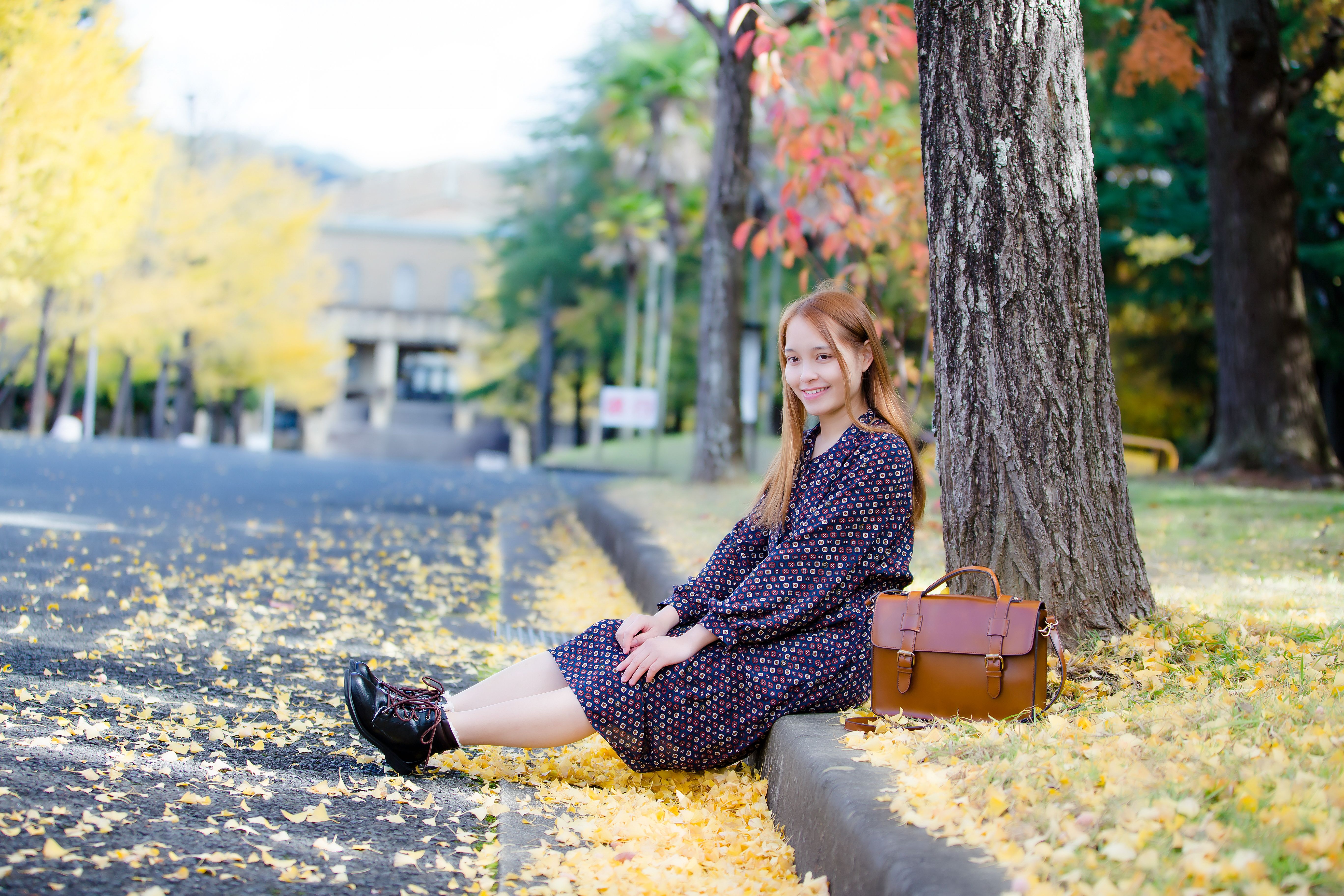 Young woman sitting under a tree on a colorful autumn day with fallen leaves.