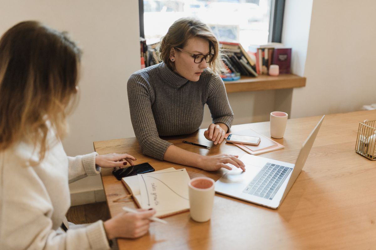 Two women working together with a laptop and notebooks in a bright office