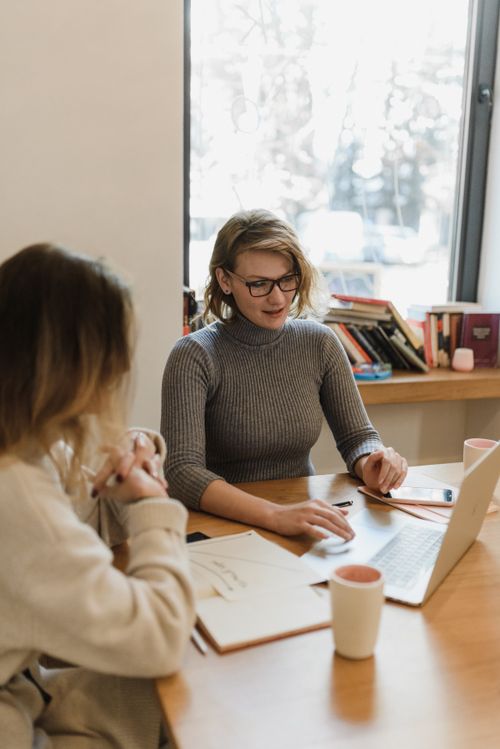 Free Two women working together on a laptop in a well-lit office setting, discussing ideas. Stock Photo