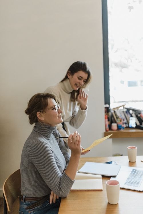 Free Two women collaborating in a modern workspace environment, exchanging ideas and documents. Stock Photo