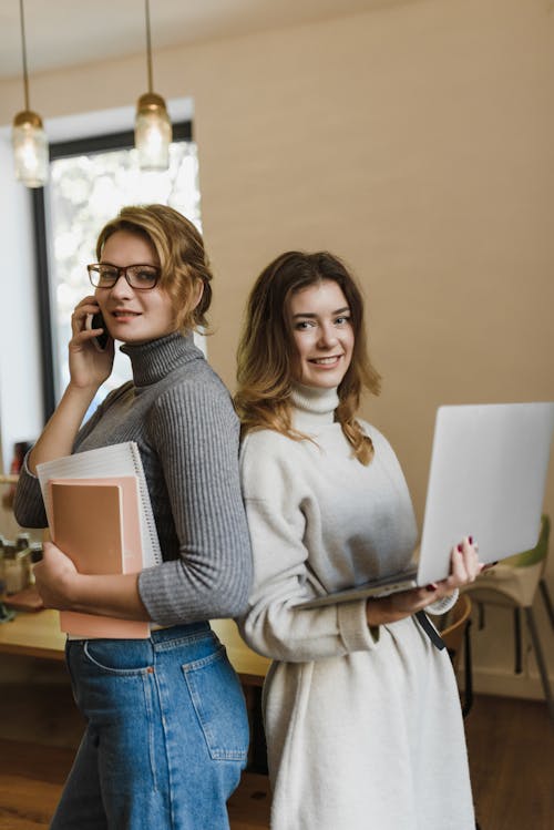 Women Standing Back to Back while Smiling at the Camera