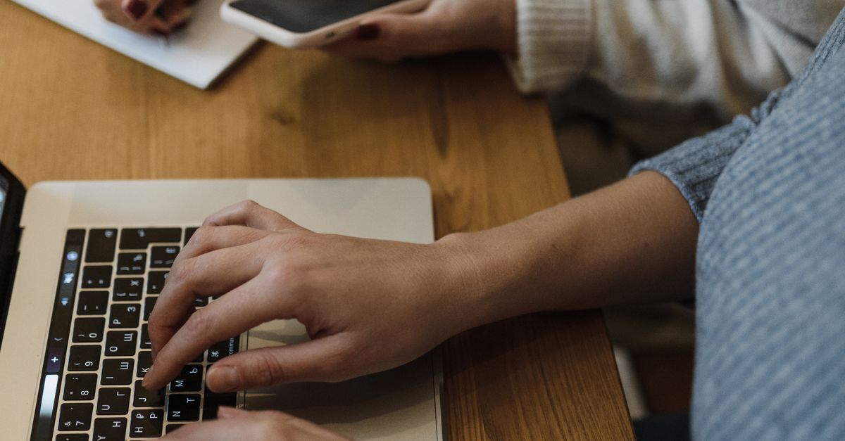 Person in Gray Sweater Typing on a Laptop Beside a Person Writing on ...