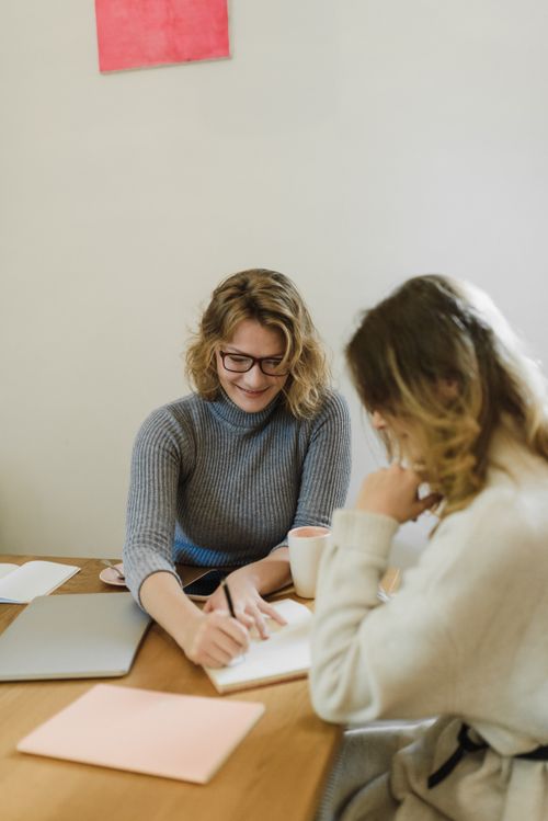 Free Two women in sweaters planning together at a wooden table with laptop and notebook. Stock Photo