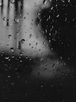 Black and white close-up of rain droplets on a glass window, creating a moody ambiance.