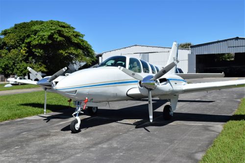 Free White twin-propeller private aircraft parked near hangar under clear blue sky. Stock Photo