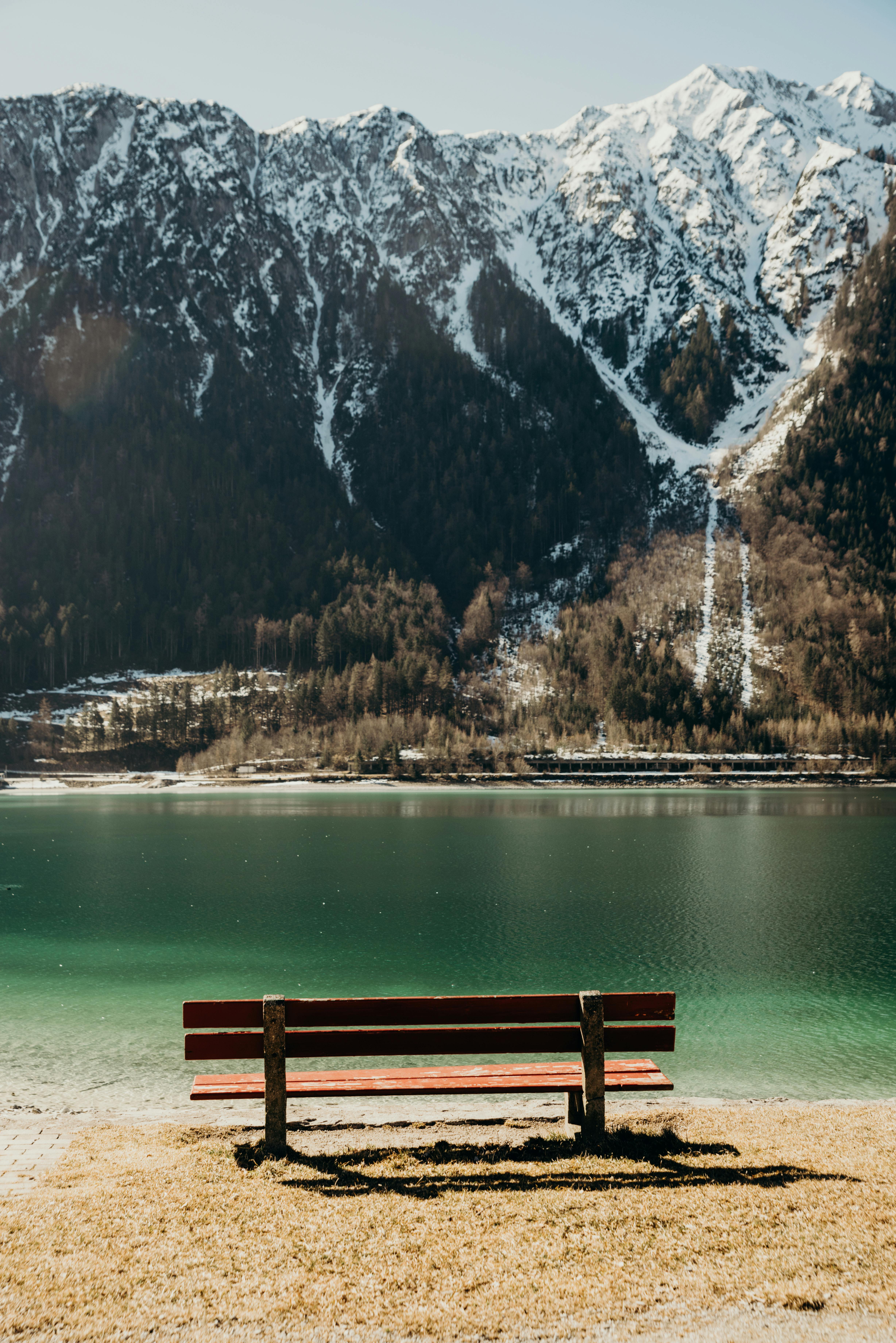 Peaceful alpine scene with a bench facing a tranquil lake and snow-capped mountains in Tyrol, Austria.