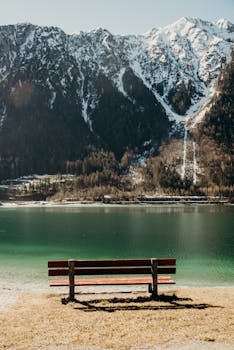 Peaceful alpine scene with a bench facing a tranquil lake and snow-capped mountains in Tyrol, Austria.