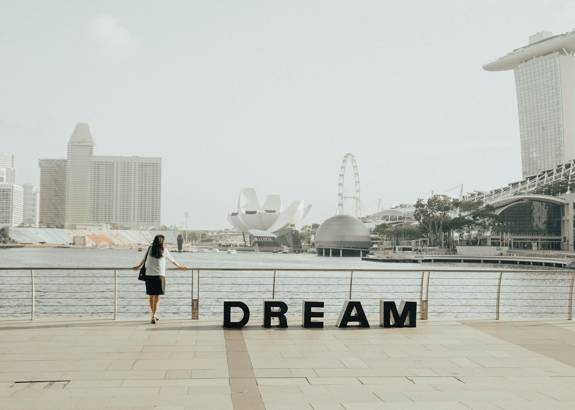 A woman gazing at the iconic Marina Bay Sands skyline in Singapore with 'Dream' letters foregrounded.