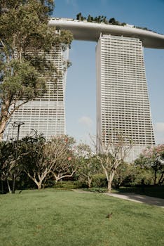 View of Marina Bay Sands towers with lush greenery in Singapore park under a blue sky.