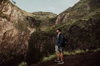 Man in Blue Jacket and Brown Shorts Standing on Rocky Mountain