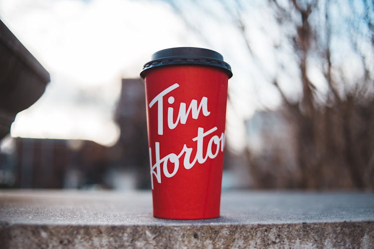 A Red Disposable Cup With Tim Horton Print On Concrete Surface