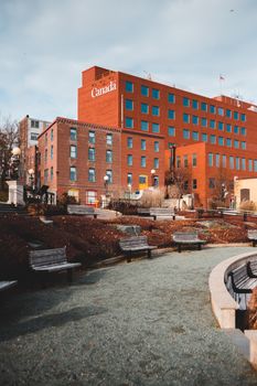 A peaceful urban park scene featuring benches, pathways, and a distinctive red brick building in the background.