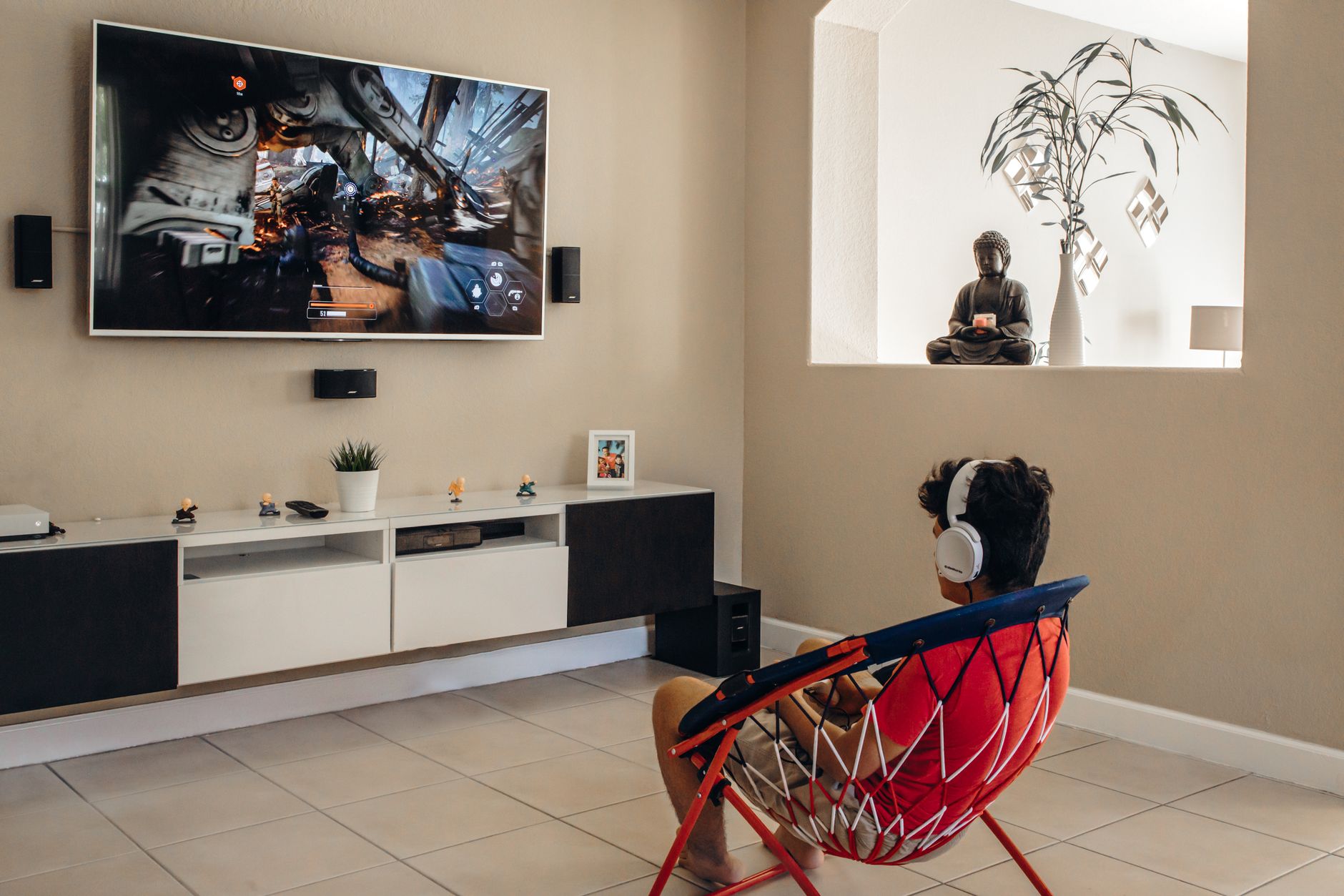 A young man wearing headphones plays video games in a modern living room setup.