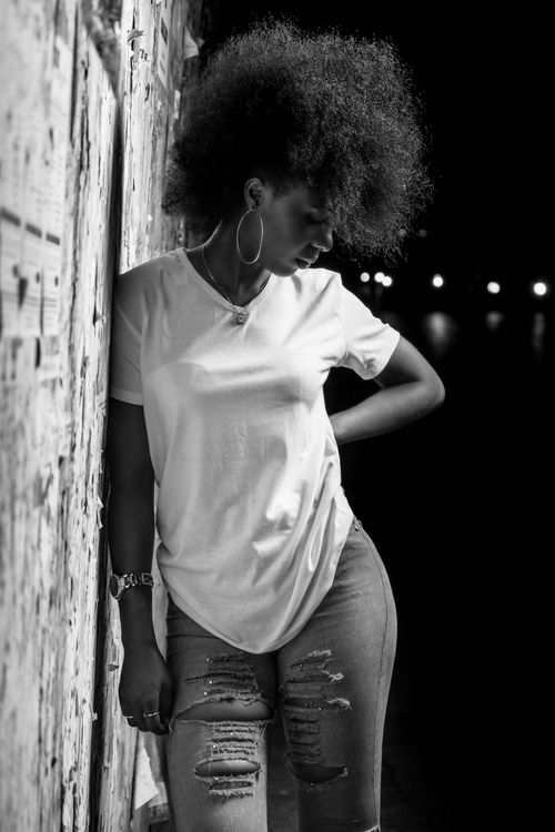 Free Black and white of young thoughtful African American female with hand on waist looking down near wall Stock Photo
