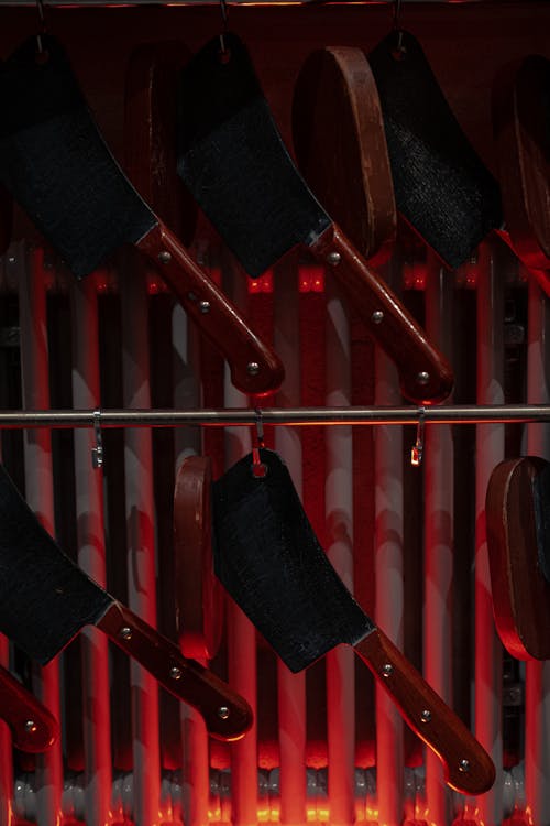 Free Heavy sharp iron knives hanging on metal rod near radiator in bright red light Stock Photo