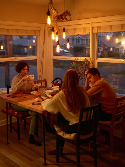 Free A group of adults enjoying a warm, cozy evening with tea and conversation in a softly lit dining room. Stock Photo