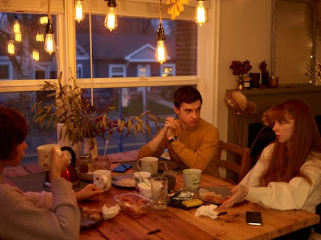 Three adults engage in a warm conversation around a dining table as evening settles in, creating a cozy home ambiance.